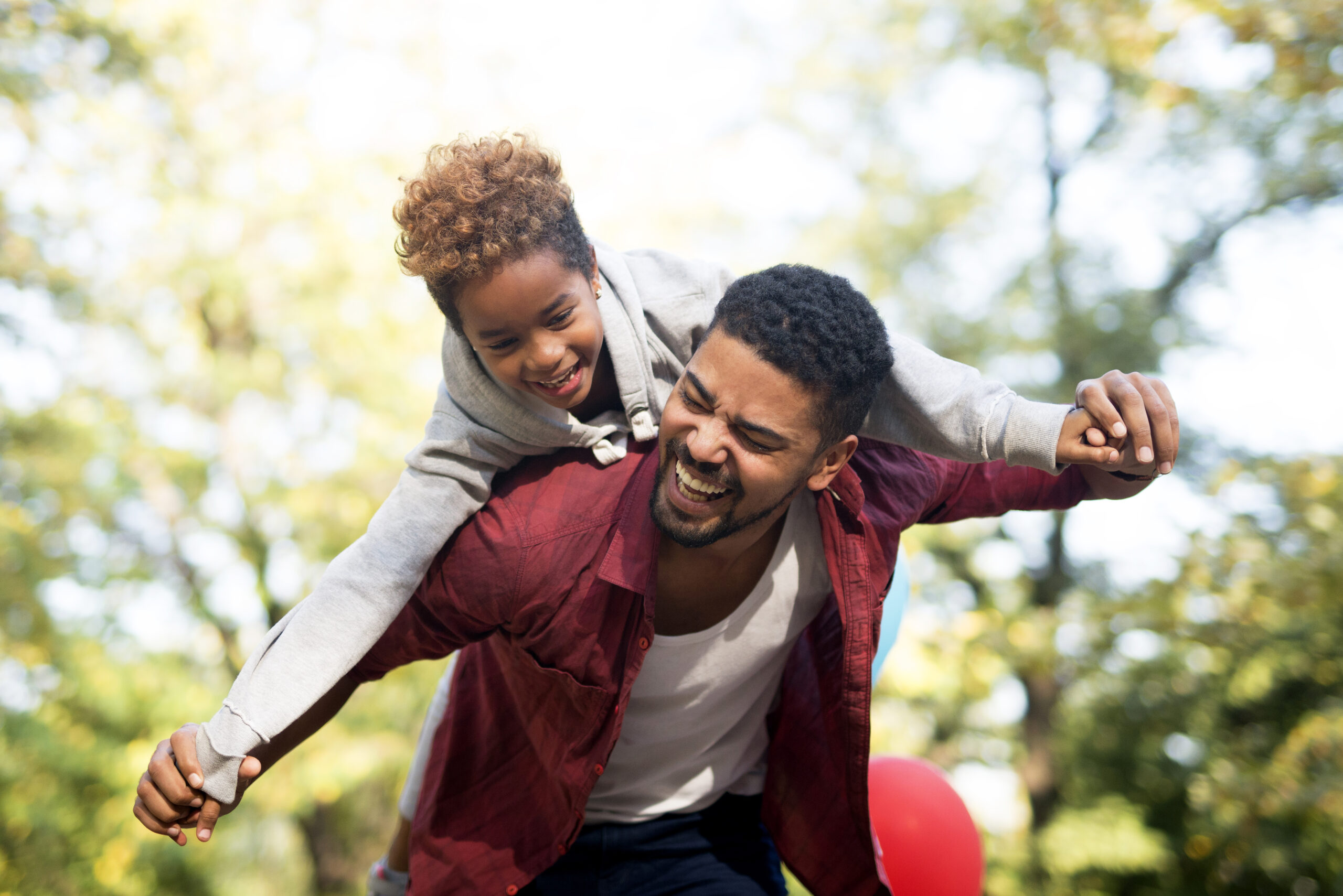 Father carrying daughter on his back with arms spread.